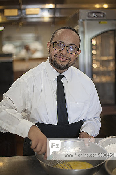 Glücklicher afroamerikanischer Mann mit Down-Syndrom kocht als Koch in einer Großküche
