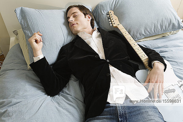 Schlafender Mann im Bett mit Gitarre.