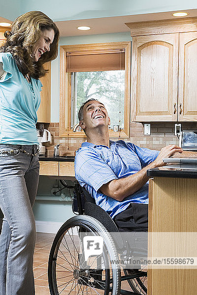 Mittlerer erwachsener Mann  der in einem Rollstuhl sitzt und eine mittlere erwachsene Frau lächelnd anschaut