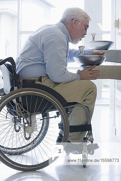 Universitätsprofessor mit Muskeldystrophie sitzt im Rollstuhl und trinkt Wasser aus einem Brunnen
