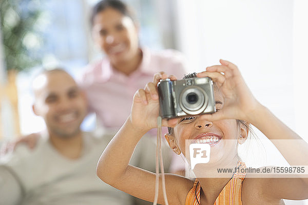 Hispanisches Mädchen  das ein Foto mit einer Digitalkamera macht  mit ihren Eltern im Hintergrund