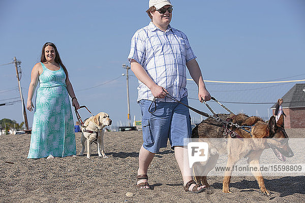 Ein blindes Paar geht mit seinen Diensthunden am Strand entlang
