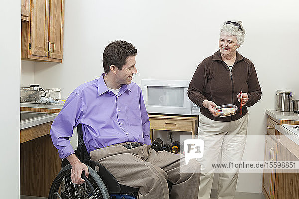 Ein Mann im Rollstuhl mit einer Rückenmarksverletzung bekommt Essen von seiner Haushaltshilfe