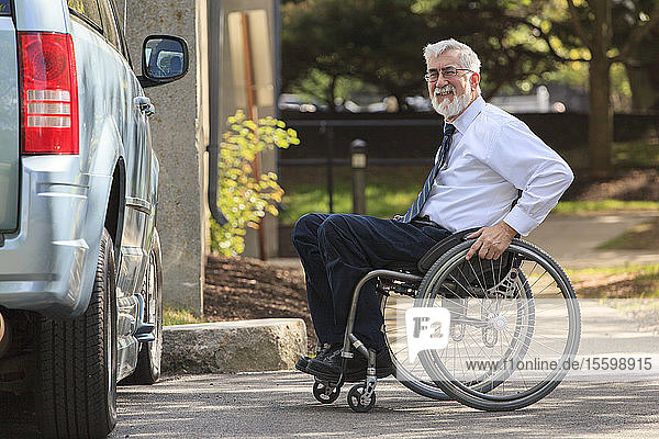 Ein Mann mit Muskeldystrophie im Rollstuhl steigt auf dem Parkplatz seines Büros in seinen behindertengerechten Wagen ein.
