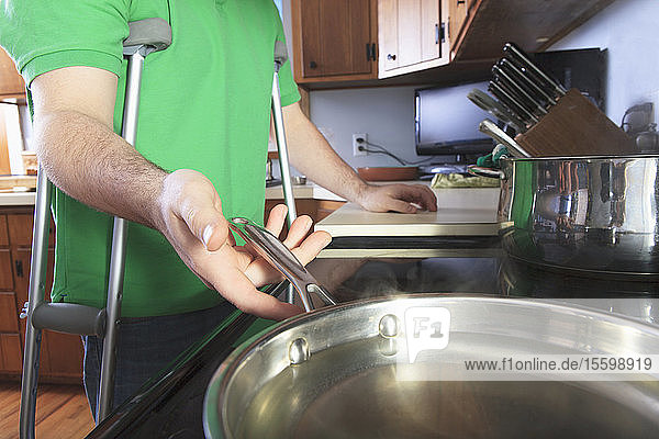 Mann nach Operation des vorderen Kreuzbandes (ACL) mit Krücken beim Kochen in der Küche