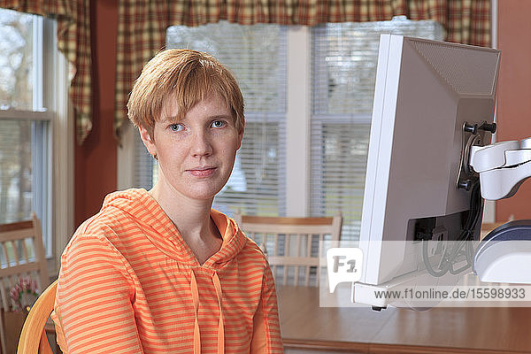 Porträt einer jungen Frau mit Sehbehinderung  die an ihrer Schreibtischlupe sitzt