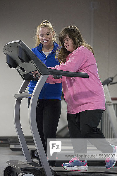 Junge Frau mit Down-Syndrom trainiert mit ihrem Trainer an einem Gerät im Fitnessstudio