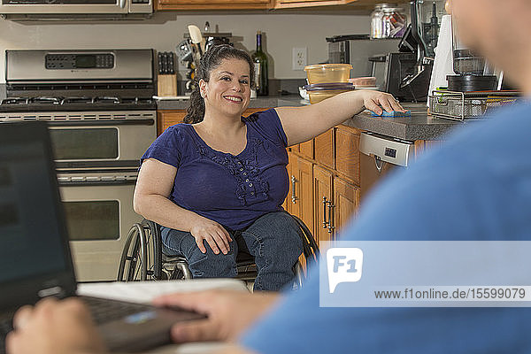 Frau mit Spina Bifida und ihr Mann benutzen Laptop in ihrer Küche