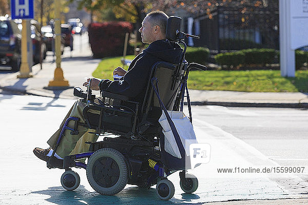 Mann mit Rückenmarksverletzung und Arm mit Nervenschaden in motorisiertem Rollstuhl überquert öffentliche Straße