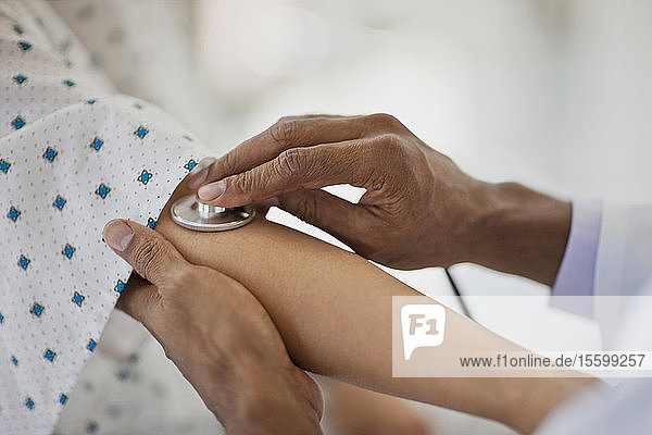 Die Hände eines Arztes  der ein Stethoskop auf die Innenseite des Ellenbogens eines Patienten setzt  um dessen Herzschlag abzuhören