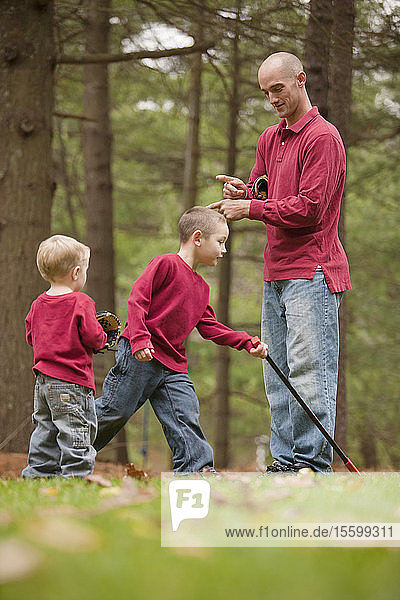 Ein Mann gebärdet das Wort Vorsicht in amerikanischer Gebärdensprache  während er mit seinen Söhnen in einem Park kommuniziert