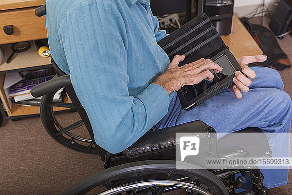 Mann mit Friedreich-Ataxie im Rollstuhl  der mit deformierten Händen ein Tablet benutzt