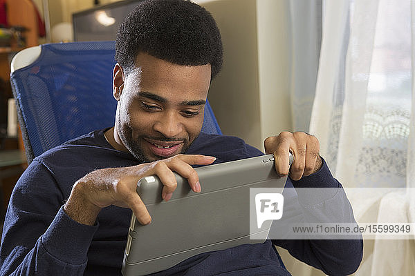 Glücklicher afroamerikanischer Mann mit zerebraler Lähmung  der zu Hause sein Tablet benutzt