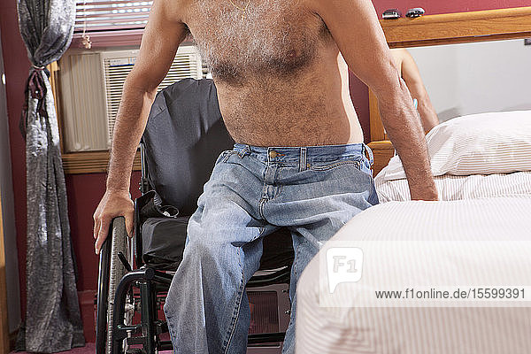 Ein Mann mit einer Rückenmarksverletzung steigt aus seinem Rollstuhl ins Bett