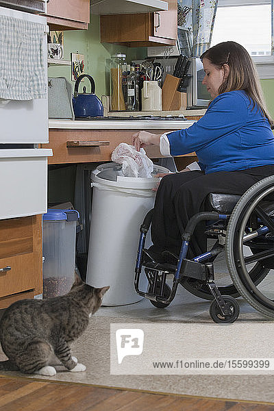 Frau mit Spina Bifida im Rollstuhl bei der Vorbereitung der Fütterung einer Katze in der barrierefreien Küche