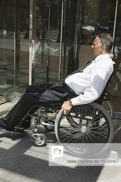 Seitenprofil eines mittleren Erwachsenen  der im Rollstuhl sitzt und versucht  eine Drehtür zu öffnen