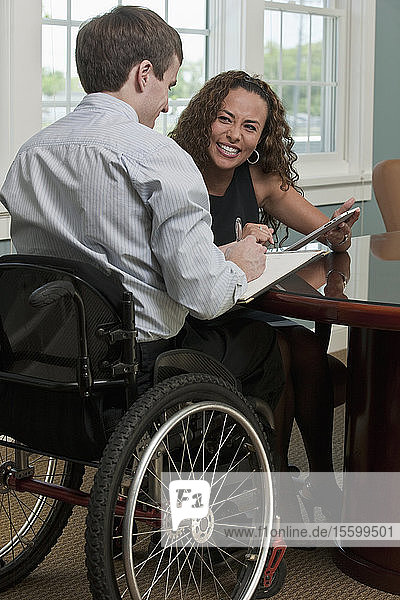 Geschäftsmann mit Rückenmarksverletzung und eine sehbehinderte hispanische Geschäftsfrau diskutieren in einem Büro