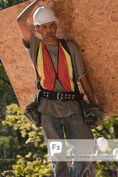 Zimmermann trägt eine Spanplatte auf einer Baustelle