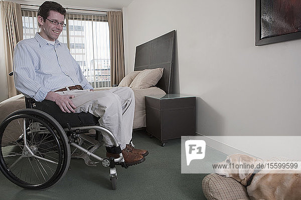 Mann im Rollstuhl mit einer Rückenmarksverletzung mit einem Diensthund im Schlafzimmer