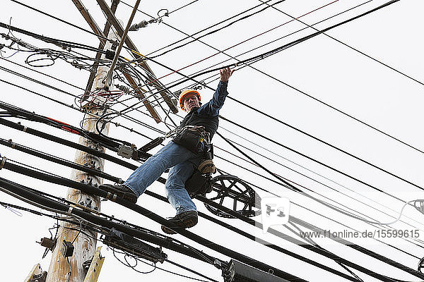 Kommunikationsmitarbeiter auf einem Strommast beim Anbringen von Klammern für das Kabel