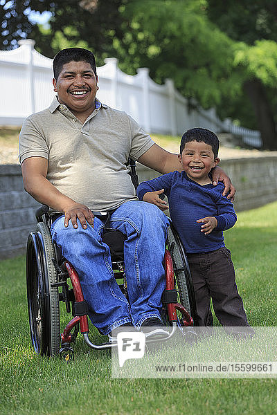 Porträt eines hispanischen Mannes mit Rückenmarksverletzung im Rollstuhl mit seinem Sohn im Rasen