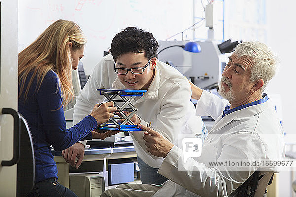 Professor mit Muskeldystrophie bei der Arbeit mit Ingenieurstudenten  die eine verstellbare Bühne an einem chemischen Analysegerät in einem Labor einrichten
