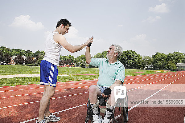 Mann mit Muskeldystrophie schüttelt einem Läufer auf einer Rennstrecke die Hand
