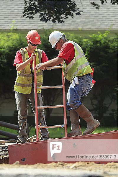 Bauarbeiter steigen über Leitern in den Verbau hinab