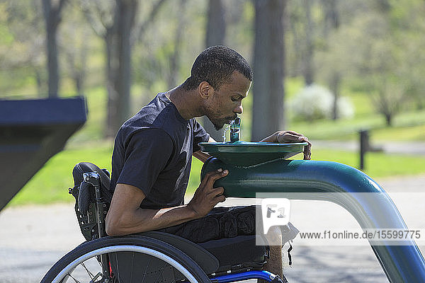 Mann im Rollstuhl  der an Spinaler Meningitis erkrankt war  benutzt einen öffentlichen Wasserbrunnen