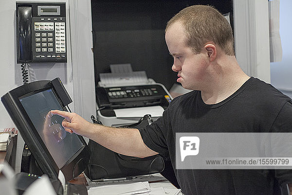 Waiter with Down Syndrome entering a sale on the computer in office