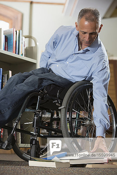 Mann im Rollstuhl mit einer Rückenmarksverletzung  der in einer Bibliothek Bücher aufhebt