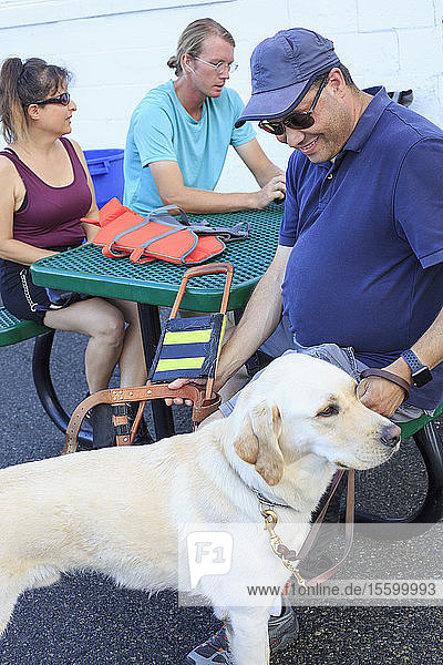 Ein blinder Mann und eine blinde Frau sitzen mit einem Diensthund und einem Segellehrer zusammen