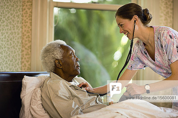 Eine Krankenschwester prüft mit einem Stethoskop den Herzschlag eines älteren Mannes  der in einem Bett sitzt