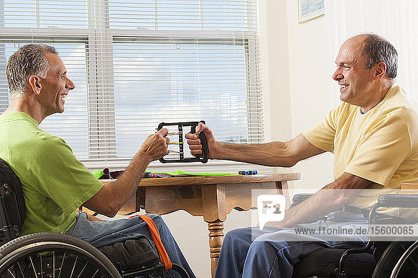 Zwei behinderte Männer sitzen in Rollstühlen und benutzen Handkraftgeräte
