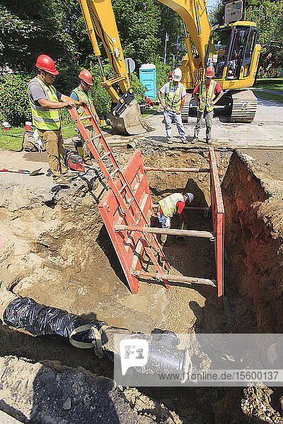Bauarbeiter messen die Länge eines Rohrs  während sie durch einen Stützpfeiler geschützt sind