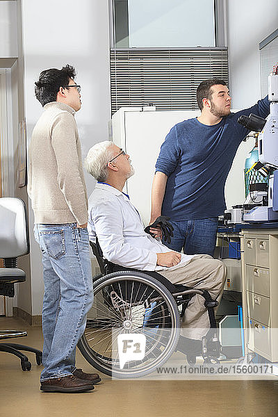 Professor mit Muskeldystrophie arbeitet mit Studenten der Ingenieurwissenschaften an der Einstellung der Kamera eines Röntgenfluoreszenzanalysegeräts in einem Labor
