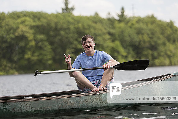 Glücklicher junger Mann mit Down-Syndrom rudert ein Kanu auf einem See
