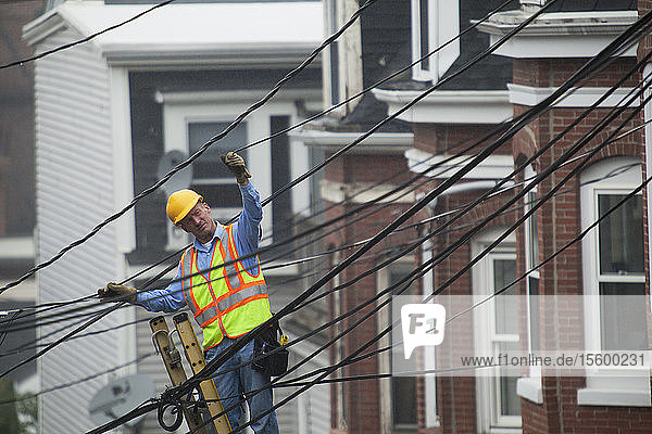 Cable lineman stretching a cable in the city from ladder