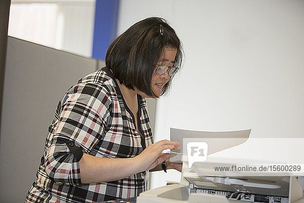 Asiatische Frau mit einer Lernbehinderung arbeitet an einem Kopiergerät im Büro