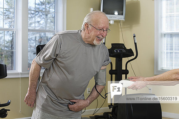 Ein älterer Mann prüft in der Turnhalle seinen Blutdruck.