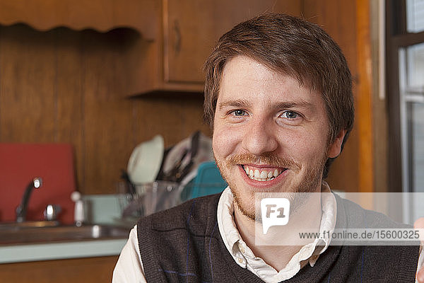 Junger blinder Mann sitzt in seiner Küche und lächelt