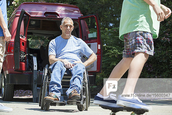Mann mit Rückenmarksverletzung im Rollstuhl beobachtet seinen Sohn auf dem Skateboard