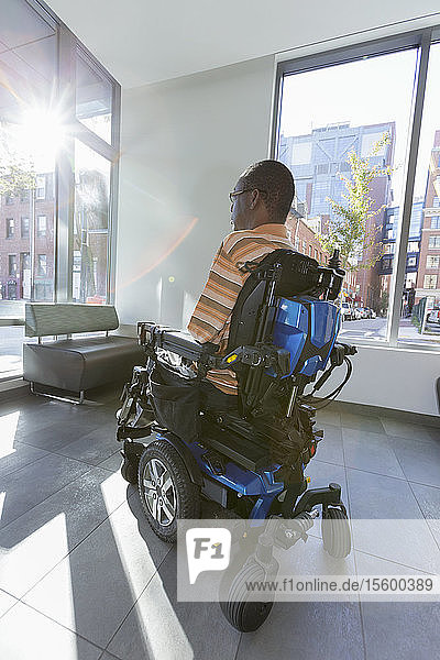 Man with Guillain-Barre Syndrome on wheelchair looking out through the apartment window
