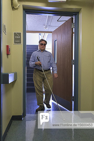 Ein Mann mit angeborener Blindheit benutzt seinen Stock  um durch eine Tür zu gehen