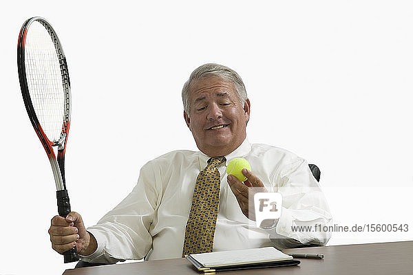 Nahaufnahme eines Geschäftsmannes  der an einem Schreibtisch sitzt und einen Tennisball betrachtet