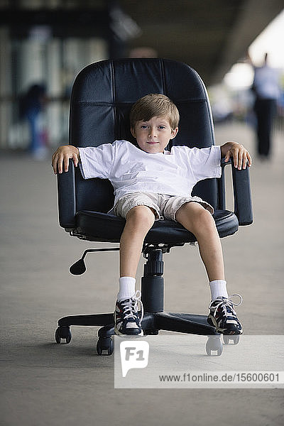 Portrait of a boy sitting in an executive chair.