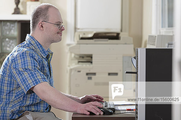 Mann mit Down-Syndrom bei der Arbeit an einem Computer in einem Büro