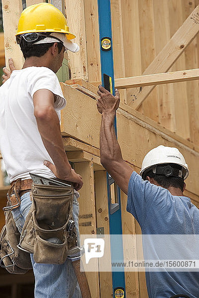 Spanische Zimmerleute messen einen Rahmen mit einer Wasserwaage an einem im Bau befindlichen Haus
