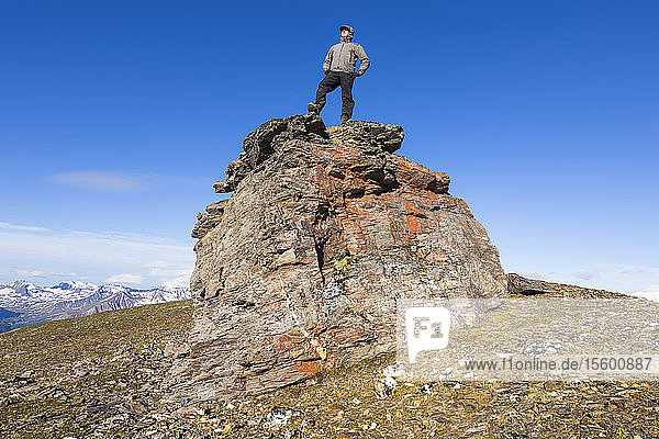 A hiker poses atop a boulder on a ridge in the Alaska Range; Alaska  United States of America