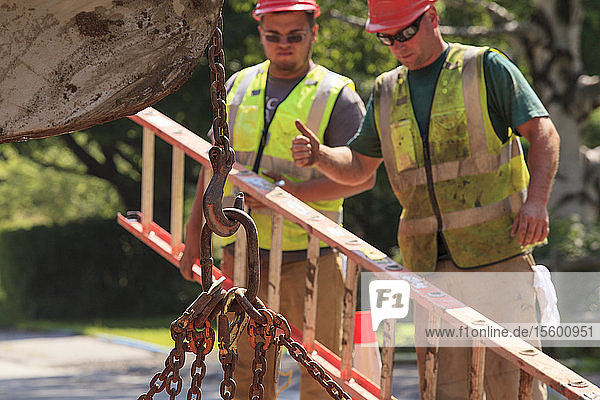 Construction workers signaling excavator operator lifting chain